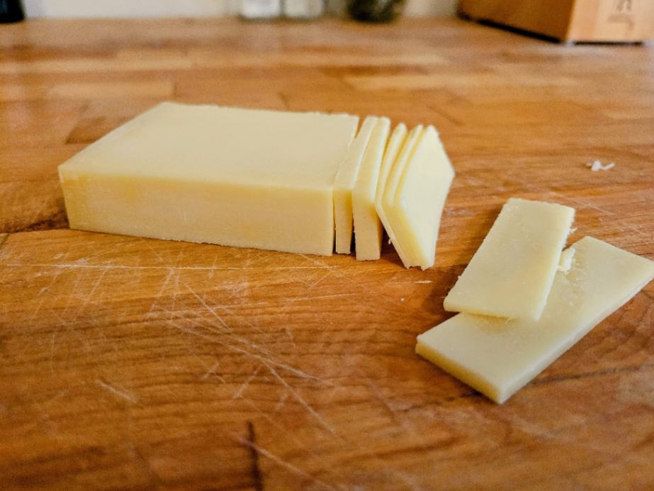 Gruyère cheese block and slices on cutting board