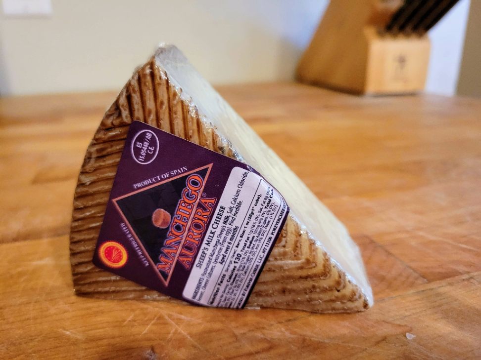 Manchego cheese in wrapper on butcher block counter