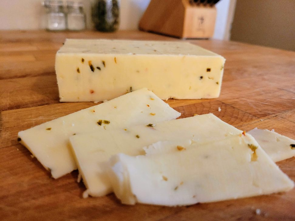 Pepperjack cheese block with slices on butcher block